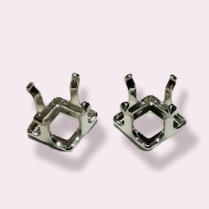 May include: Two silver metal settings for a square-shaped gemstone. The settings have four prongs each and are designed to hold a stone securely in place.