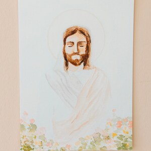 May include: Watercolour painting of a figure with closed eyes, brown hair, and a beard, surrounded by a halo. The figure is wearing a white robe with peach-coloured accents. The bottom of the painting features a floral border with green and pink hues.