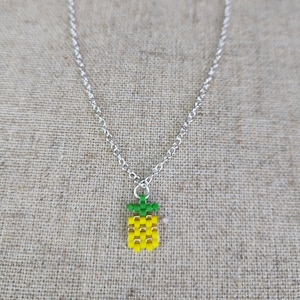 May include: A silver chain necklace with a small pineapple charm made of yellow and green beads.