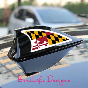 May include: Black car antenna with a Maryland state flag decal. The flag is yellow, black, and red with a white background.