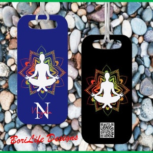 May include: Two luggage tags with a white silhouette of a person meditating in a colorful mandala. The tag on the left is blue with the letter N and the text "Nayda". The tag on the right is black with a QR code.