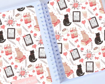 May include: A white notebook with a spiral binding. The cover features a repeating pattern of cats, books, coffee cups, and hearts. The text "Laura's Stickers" is printed on the bottom of the cover.