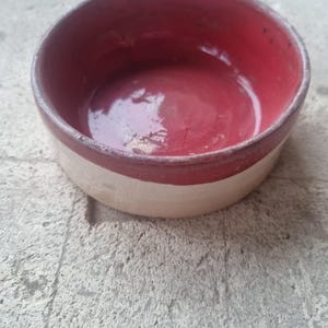May include: A small, red and white ceramic bowl. The bowl is glazed and has a smooth, rounded shape.