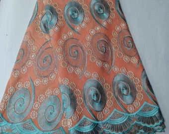 May include: Peach colored fabric with a turquoise embroidered design of swirling patterns. The fabric has a scalloped edge.
