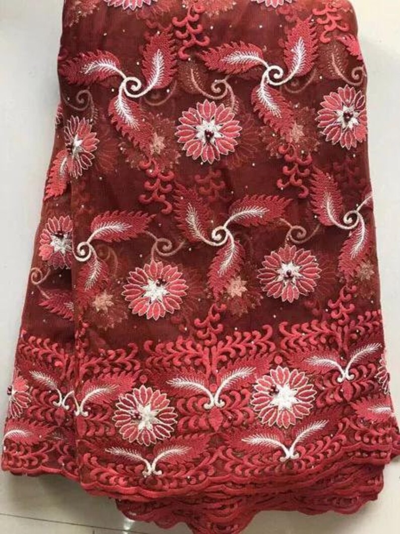 May include: Burgundy lace fabric with a floral and leaf pattern. The design features embroidered flowers and leaves in shades of red and white. The fabric is semi-sheer, with a delicate texture, suitable for apparel or craft projects.