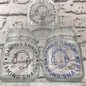 May include: Three clear glass jars with black lids and labels that say "Gaming Snacks" with a blue headset icon.
