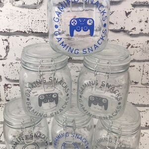 May include: Five clear glass jars with airtight lids. Each jar has a blue and gray sticker with the text "Gaming Snacks" and a graphic of a video game controller or headphones.