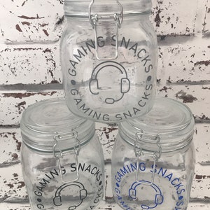 May include: Three clear glass jars with silver lids and a blue and gray graphic that says "Gaming Snacks" around a headset icon.