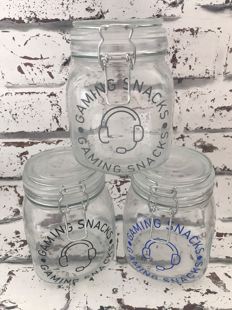 May include: Three clear glass jars with silver lids and a blue and gray graphic that says "Gaming Snacks" around a headset icon.