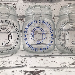 May include: Three clear glass jars with black lids and labels that say "Gaming Snacks" with a blue headset icon in the center.