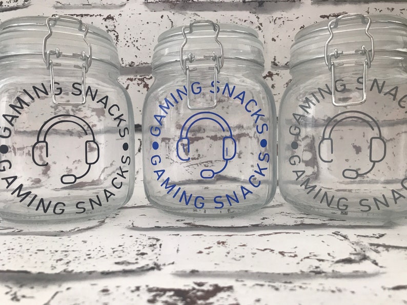 May include: Three clear glass jars with black lids and labels that say "Gaming Snacks" with a blue headset icon in the center.