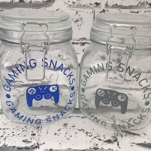 May include: Two clear glass jars with silver lids and blue and gray gamer controller graphics. The jars are labeled "Gaming Snacks".