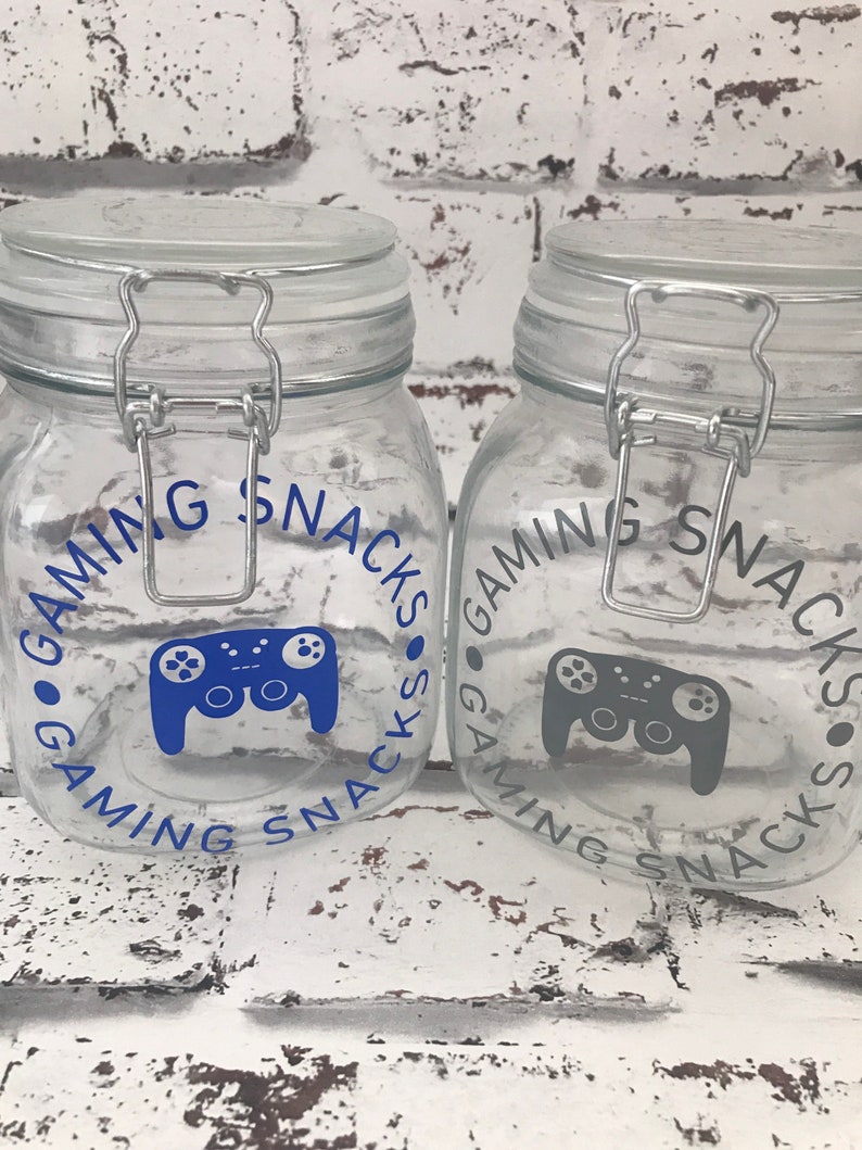 May include: Two clear glass jars with silver lids and blue and gray gamer controller graphics. The jars are labeled "Gaming Snacks".