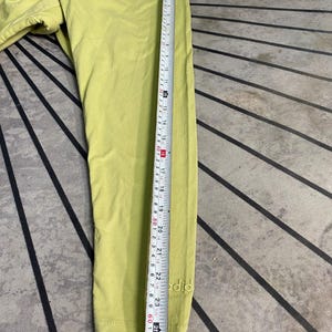 May include: A lime green long-sleeve shirt featuring the word "did" embroidered in a matching thread near the cuff. A white measuring tape is placed along the sleeve, indicating a length of approximately 24.5 inches from the shoulder seam.