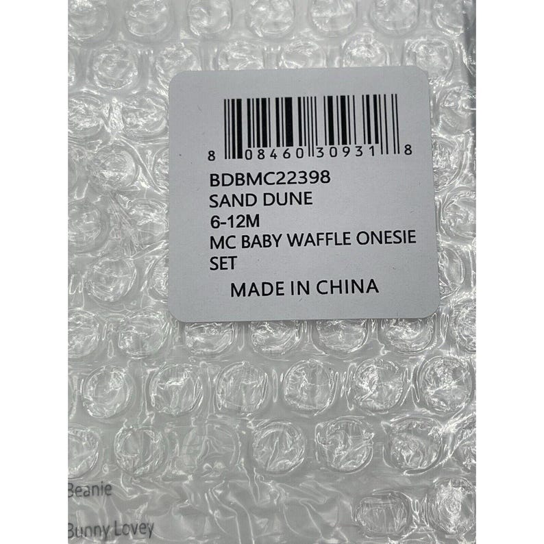 Pu&ograve; includere: Un'etichetta bianca con un codice a barre, codice prodotto BDBMC22398, colore DUNA DI SABBIA, taglia 6-12 mesi, descrizione SET DI BODY A GOFRE PER BAMBINI MC, e PRODOTTO IN CINA.