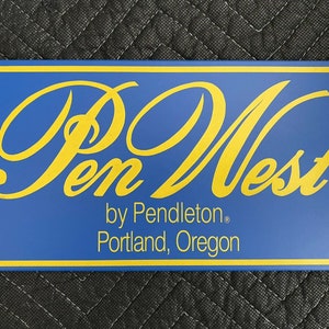 Puede incluir: Un letrero azul y dorado con el texto "Pen West by Pendleton, Portland, Oregon" y un símbolo de marca registrada.