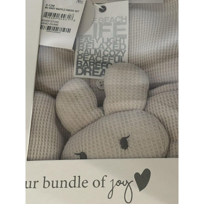 Pu&ograve; includere: Un set di body in waffle grigio per neonati con un giocattolo di peluche a forma di coniglio. La confezione presenta il testo "Beach Life" e "Easy Light Relaxed Calm Cozy Peaceful Barefoot Dream".