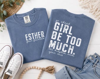 Puede incluir: Dos camisetas azules de manga corta. La camiseta de la izquierda tiene el texto blanco ESTHER four:fourteen. La de la derecha tiene el texto blanco go ahead GIRL BE TOO MUCH. the kingdom needs your voice. Ambas tienen un estilo desgastado.