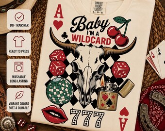 Puede incluir: Una camiseta color crema con un estampado gráfico de un cráneo de buey, dados rojos, cerezas, una bola de discoteca, un encendedor y labios rojos. El texto dice Baby I'M A WILDCARD y 777. El diseño incluye símbolos de cartas de as y un patrón de cuadros.