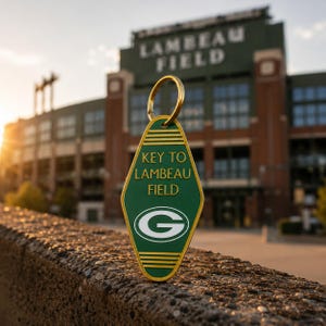 Op de afbeelding: Een ruitvormige, groene sleutelhanger in hotelstijl met een gouden rand en een gouden metalen ring. De tekst KEY TO LAMBEAU FIELD staat in gouden letters boven een wit en groen G-logo. De sleutelhanger heeft horizontale gouden lijnen.