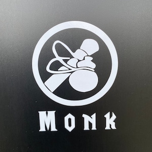 May include: A white circle with a black outline containing a stylized image of a monk's bag. The word "MONK" is written in white below the circle.