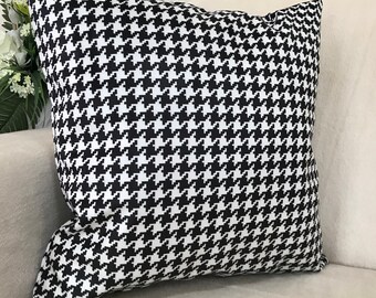 Puede incluir: Cojín decorativo cuadrado con un patrón de pata de gallo en blanco y negro. El cojín está hecho de una tela suave y está colocado sobre una superficie de color claro. Es un artículo de decoración del hogar.