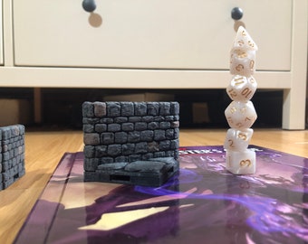 May include: A stack of white dice with gold numbers on a purple book with the word "Master's" visible. Two gray stone wall miniature models are on the book.