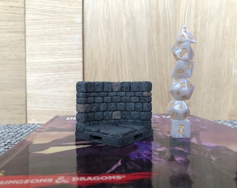 May include: A miniature stone wall with a small platform, and a stack of six white dice with gold numbers, on a book with the text "Dungeons & Dragons".