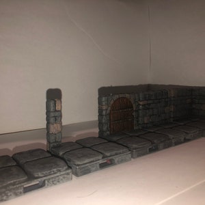 May include: A set of grey stone dungeon tiles featuring a brown wooden door and stone archway. The tiles are designed for tabletop role-playing games.
