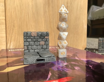 May include: A white stone wall miniature with a stack of five white dice with gold numbers on top. The dice are a d4, d6, d8, d10, and d20.