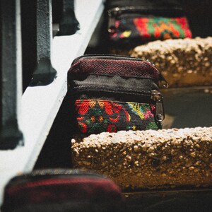 May include: Three small zippered pouches with colorful floral patterns on a set of concrete stairs. The pouches are black with red, yellow, and green floral designs.