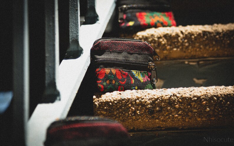May include: Three small zippered pouches with colorful floral patterns on a set of concrete stairs. The pouches are black with red, yellow, and green floral designs.