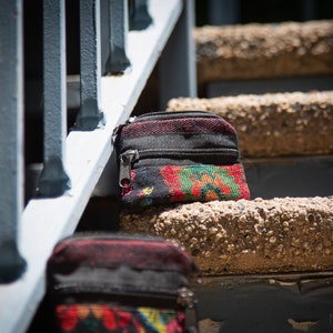 May include: Two small black zippered pouches with colorful floral patterns. The pouches are sitting on a set of concrete steps.