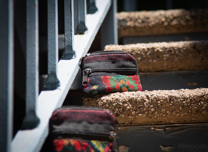 May include: Two small black zippered pouches with colorful floral patterns. The pouches are sitting on a set of concrete steps.