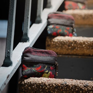 May include: A small black zippered pouch with a red, yellow, and green floral pattern. The pouch is sitting on a concrete step.