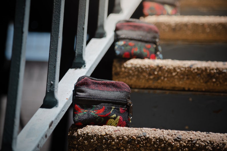 May include: A small black zippered pouch with a red, yellow, and green floral pattern. The pouch is sitting on a concrete step.