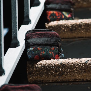 May include: A small black and red patterned pouch with a zipper closure. The pouch is sitting on a concrete step.