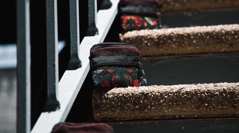 May include: A small black and red patterned pouch with a zipper closure. The pouch is sitting on a concrete step.