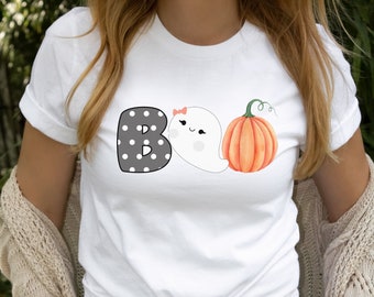 May include: White t-shirt with a black and white polka dot "B", a white ghost with a pink bow, and an orange pumpkin. The text "BOO" is displayed on the shirt.
