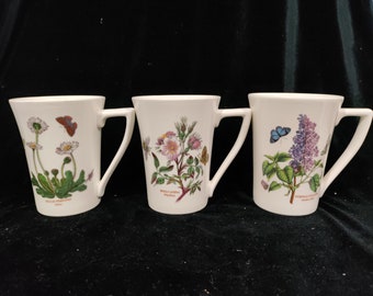 May include: Three white ceramic mugs with floral designs and butterfly illustrations. The mugs feature the names "Bellis Perennis", "Rosa Canina", and "Syringa Vulgaris" with their corresponding Latin names.
