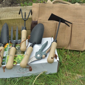 May include: A set of gardening tools with wooden handles and a brown canvas bag. The tools include a trowel, a hand rake, a cultivator, a hand fork, a pair of pruning shears, and a hoe. The tools are packaged in a white box with the text "Easylife Pro" printed on it.