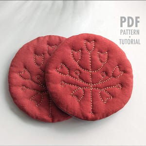 Pode incluir: Duas bases redondas de tecido vermelho com um desenho floral costurado. As bases são feitas de um material texturizado e apresentam um padrão costurado em creme. O texto "PDF PATTERN TUTORIAL" está no canto superior direito.