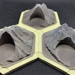 May include: Three gray, 3D printed, hexagonal volcano terrain tiles with a crater in the center of each. The tiles are designed for use in tabletop games and have a textured surface.