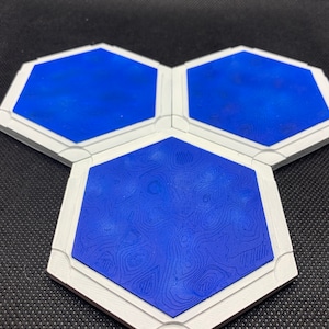 Può includere: Tre piastrelle esagonali con bordo bianco e superficie blu. La piastrella centrale presenta un motivo testurizzato, mentre le altre due piastrelle hanno una superficie liscia.