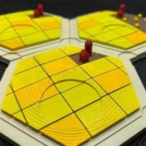 Op de afbeelding: Een set van drie zeshoekige speltegels in geel en beige. Elke tegel toont een gestileerd veld met verschillende tinten geel, en kleine rode structuren. De tegels zijn ontworpen voor een bordspel.