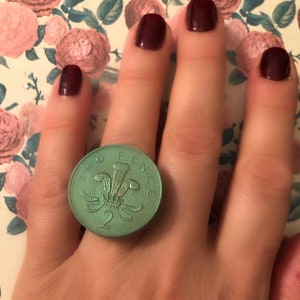 May include: A green two pence coin ring with the inscription "Two Pence" and a royal crest.
