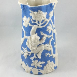 May include: A blue and white ceramic vase with a raised design of a person climbing a tree. The vase has a scalloped rim.