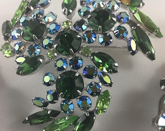 May include: A vintage brooch with a floral design. The brooch features a cluster of green, blue, and clear crystals set in a silver-tone metal. The crystals are various shapes and sizes, including round, oval, and marquise.