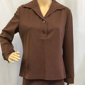 May include: A brown skirt suit with a collared top and three buttons. The skirt is knee-length and the top has long sleeves.