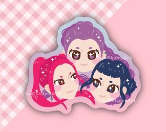 Peut inclure: Un autocollant représentant trois visages féminins stylisés avec des cheveux roses, violets et bleus. L'autocollant a une bordure blanche et est posé sur un fond rose à carreaux.